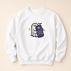 May include: A white crewneck sweatshirt featuring an embroidered design of a white ghost holding a purple beverage can with a skull icon and the text custom name. The design includes small green star accents and a small black bat above the can.