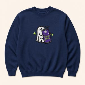 May include: A navy blue crewneck sweatshirt featuring an embroidered design of a white ghost holding a purple can. The can displays a white skull icon and the text custom name in lime green, surrounded by small lime green star accents.