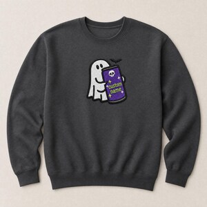 May include: A dark grey crewneck sweatshirt featuring an embroidered design of a white ghost holding a purple beverage can. The can displays a small white skull icon, yellow star accents, and the text custom name in lime green lettering.