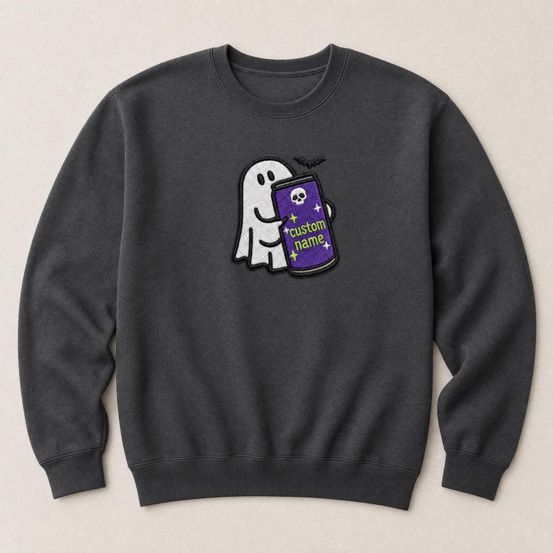 May include: A dark grey crewneck sweatshirt featuring an embroidered design of a white ghost holding a purple beverage can. The can displays a small white skull icon, yellow star accents, and the text custom name in lime green lettering.