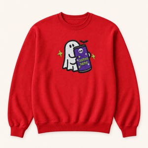 May include: A red crewneck sweatshirt featuring an embroidered design of a white ghost holding a purple can. The can displays a skull icon, the text "custom name" in green, and small star accents. A small black bat is positioned above the ghost.