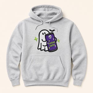 May include: A light grey hooded sweatshirt featuring an embroidered graphic of a white ghost holding a purple can with a skull icon and the text custom name. The design includes a small black bat and four lime green four-pointed stars.
