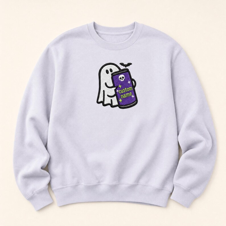 May include: A light purple crewneck sweatshirt featuring a central embroidered graphic of a white ghost holding a purple energy drink can. The can displays a small white skull icon, yellow star accents, and the text custom name in green.