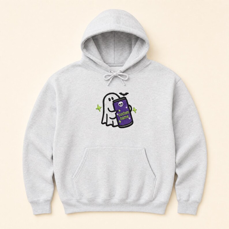 May include: A light grey hooded sweatshirt featuring a central embroidered graphic of a white ghost holding a purple beverage can. The can displays a small skull icon, the text "custom name", and is surrounded by small green star accents.