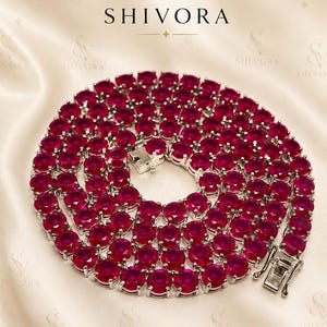 Puede incluir: Un collar de tenis circular con numerosas piedras redondas de color rojo vibrante engastadas en un marco de metal plateado pulido. El collar incluye un cierre de caja seguro y se muestra debajo del logotipo de la marca y el texto SHIVORA.