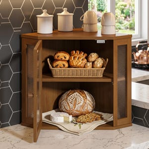May include: A wooden corner cabinet with two shelves and a glass door. The top shelf holds a woven basket filled with pastries and rolls. The bottom shelf contains a large round loaf of bread, a wedge of cheese, and crackers on a cloth napkin.