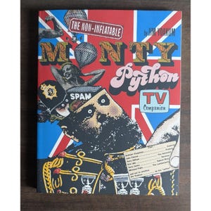 May include: A hardback book titled The Non-Inflatable Monty Python TV Companion by Jim Yoakum. The cover features a red, white, and blue Union Jack background with collage-style illustrations, including a Spam tin, a person, and text.