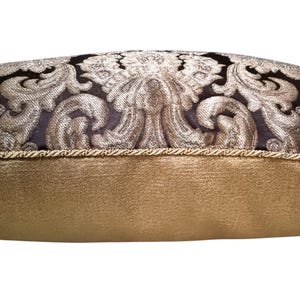 May include: A decorative pillow with a black and gold damask pattern. The pillow has a gold trim and a solid gold back.