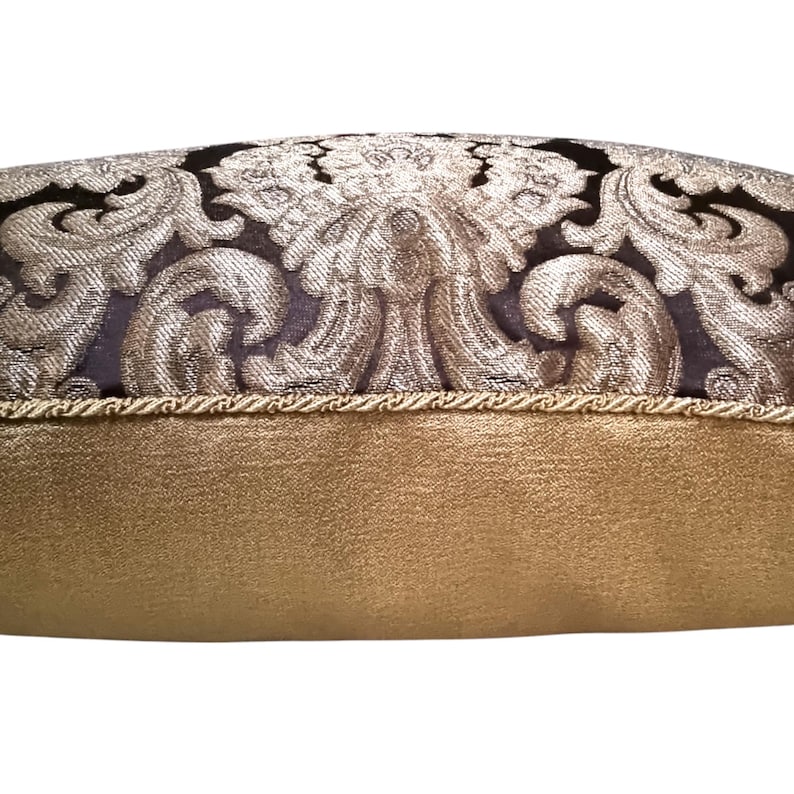 May include: A decorative pillow with a black and gold damask pattern. The pillow has a gold trim and a solid gold back.