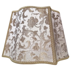 May include: A white lampshade with a gold floral pattern and a gold trim. The lampshade has a scalloped edge.
