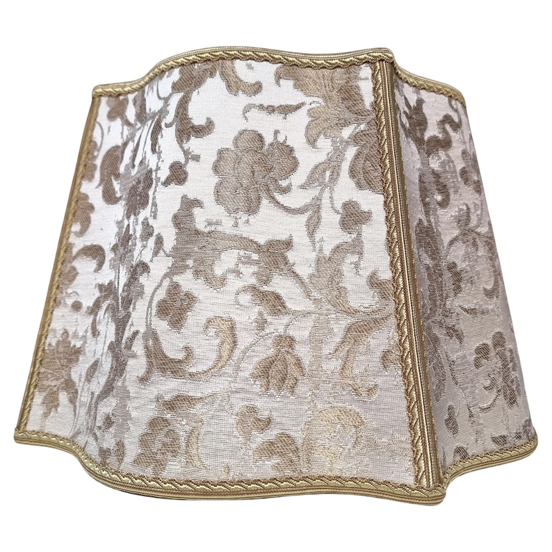 May include: A white lampshade with a gold floral pattern and a gold trim. The lampshade has a scalloped edge.