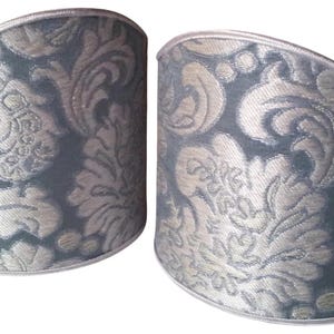 May include: Two decorative cuff bracelets with a damask pattern. The cuffs are a muted teal color with a silver-colored floral design. The edges are trimmed with a silver-colored border.