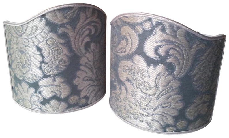 May include: Two decorative cuff bracelets with a damask pattern. The cuffs are a muted teal color with a silver-colored floral design. The edges are trimmed with a silver-colored border.