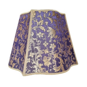 May include: A purple and gold lampshade with a floral pattern. The lampshade has a scalloped edge and a gold trim.