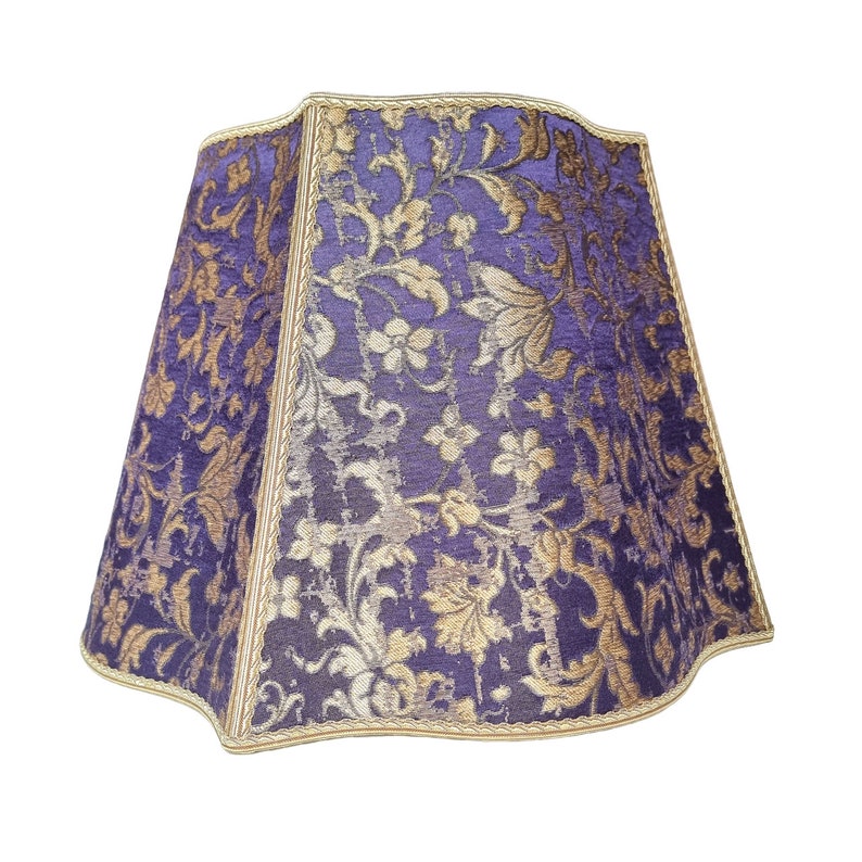May include: A purple and gold lampshade with a floral pattern. The lampshade has a scalloped edge and a gold trim.