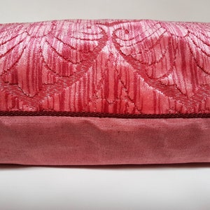 May include: A pink velvet pillow with a floral pattern and a dark red trim.