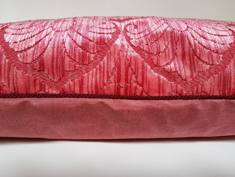 May include: A pink velvet pillow with a floral pattern and a dark red trim.