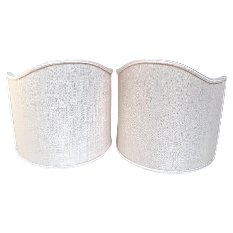 May include: A pair of off-white fabric lampshades with a curved top and a smooth, textured surface.