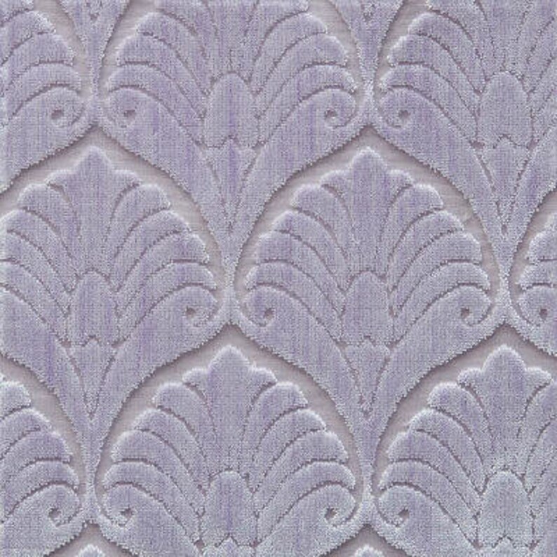 May include: A close-up of a soft, textured fabric with a repeating pattern of stylized, overlapping fan shapes. The fabric is a light purple color.