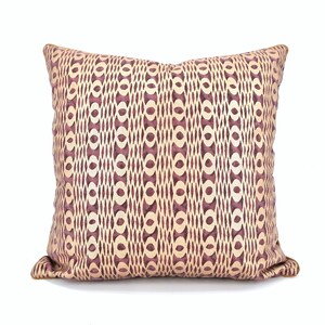 Op de afbeelding: Een decoratief kussen met een geometrisch patroon in beige en bordeaux tinten.