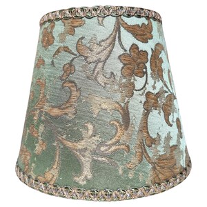 Pode incluir: Um abajur verde com um padr&atilde;o floral dourado e uma borda dourada em torno do topo e da base.