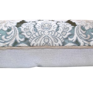 May include: A decorative cushion with a light blue and white floral pattern. The cushion has a beige trim and a white backing.