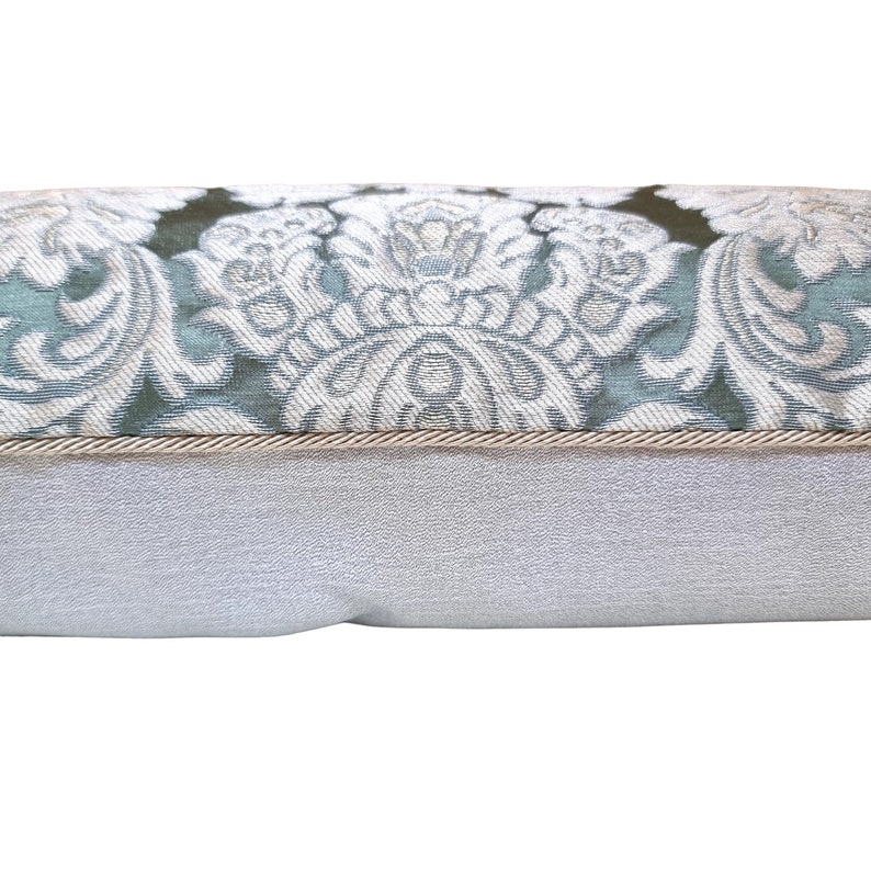 May include: A decorative cushion with a light blue and white floral pattern. The cushion has a beige trim and a white backing.