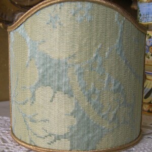May include: A light green lampshade with a floral pattern and a gold trim.