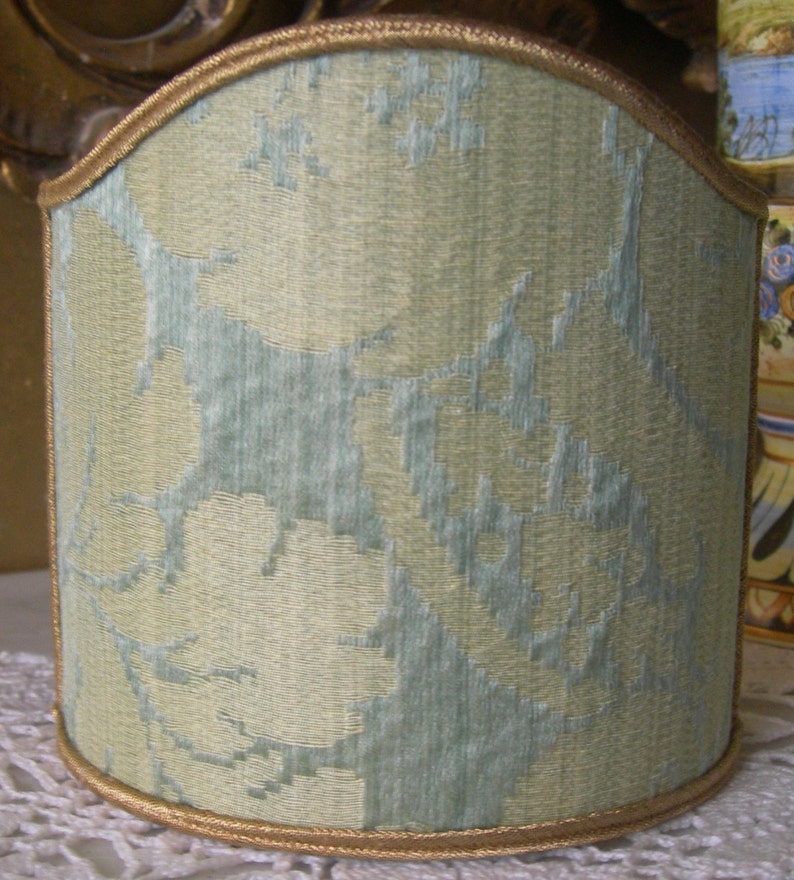 May include: A light green lampshade with a floral pattern and a gold trim.