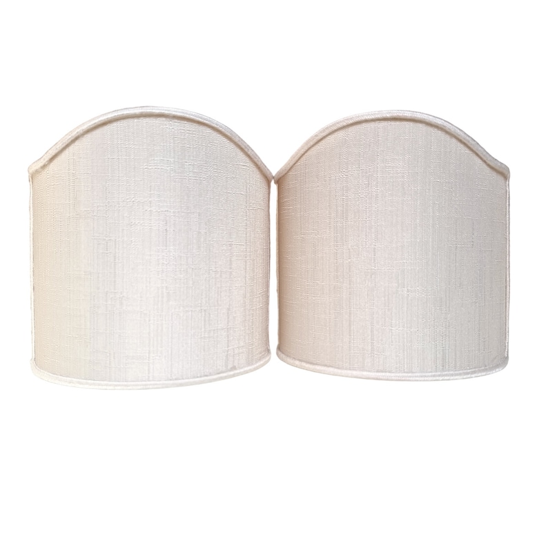 May include: Two off-white fabric lampshades with a curved top and a smooth, textured surface.