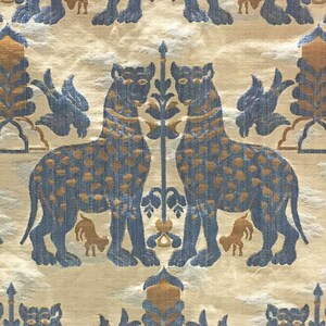 Pode incluir: Uma tape&ccedil;aria com um padr&atilde;o repetitivo de animais, p&aacute;ssaros e plantas estilizados em azul e dourado. Os animais s&atilde;o representados em p&eacute; com a cabe&ccedil;a virada para o lado. Os p&aacute;ssaros s&atilde;o representados em voo. As plantas s&atilde;o representadas de forma estilizada com folhas e flores.