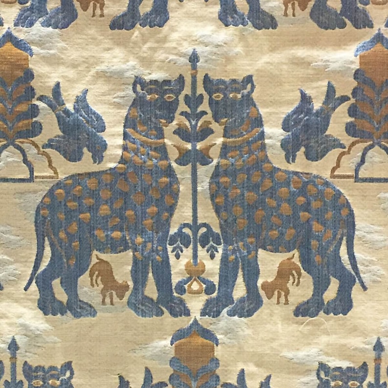 Pode incluir: Uma tape&ccedil;aria com um padr&atilde;o repetitivo de animais, p&aacute;ssaros e plantas estilizados em azul e dourado. Os animais s&atilde;o representados em p&eacute; com a cabe&ccedil;a virada para o lado. Os p&aacute;ssaros s&atilde;o representados em voo. As plantas s&atilde;o representadas de forma estilizada com folhas e flores.