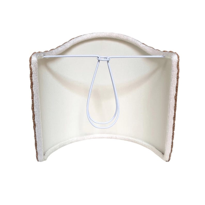 May include: A lampshade with a white interior and a brown textured border. The lampshade has a curved top and bottom, and a white metal frame for attaching to a lamp base. The shade is designed to diffuse light.