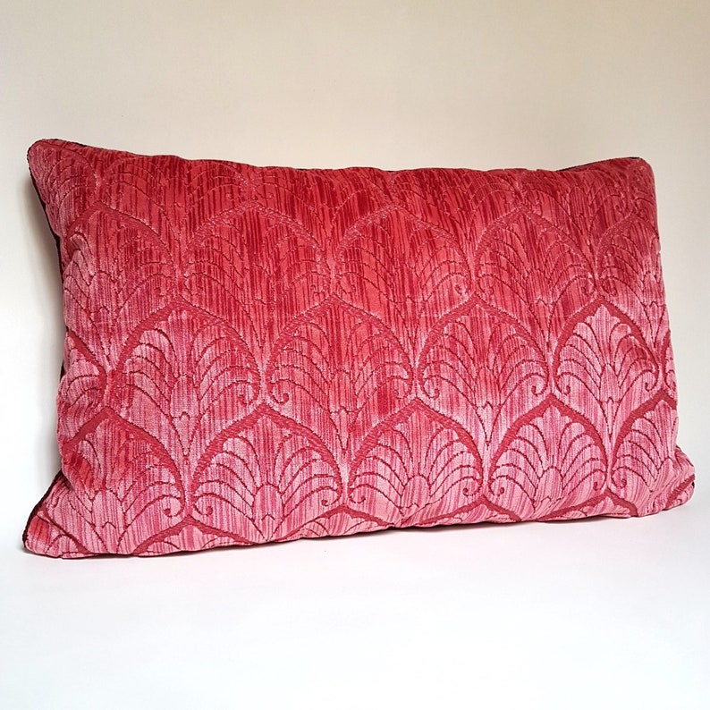 May include: A pink patterned throw pillow with a subtle sheen. The pillow has a decorative design of stylized leaves and swirls.