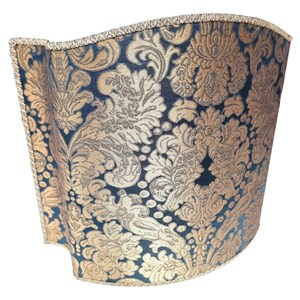 May include: A black and gold lampshade with a damask pattern. The lampshade is curved and has a gold trim.