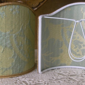 May include: Two lampshades with a green and white floral pattern. The lampshades are curved and have a gold trim.