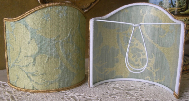 May include: Two lampshades with a green and white floral pattern. The lampshades are curved and have a gold trim.