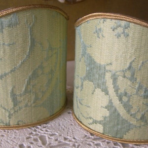 May include: Two light green lampshades with a floral pattern and gold trim.