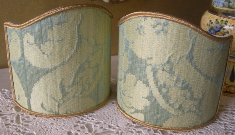 May include: Two light green lampshades with a floral pattern and gold trim.
