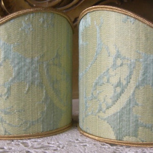 May include: Two pale green lampshades with a gold trim and a light blue floral pattern.