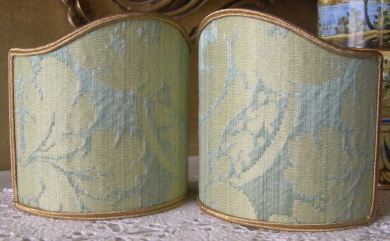 May include: Two pale green lampshades with a gold trim and a light blue floral pattern.