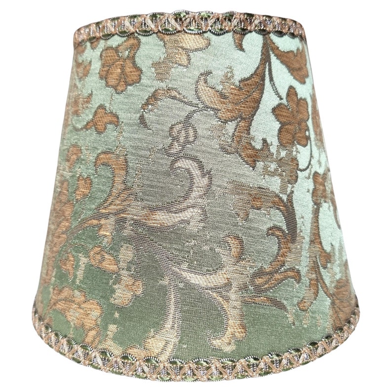 Pode incluir: Um abajur verde com um padr&atilde;o floral dourado e marrom. O abajur tem uma guarni&ccedil;&atilde;o decorativa ao redor da parte superior e inferior.