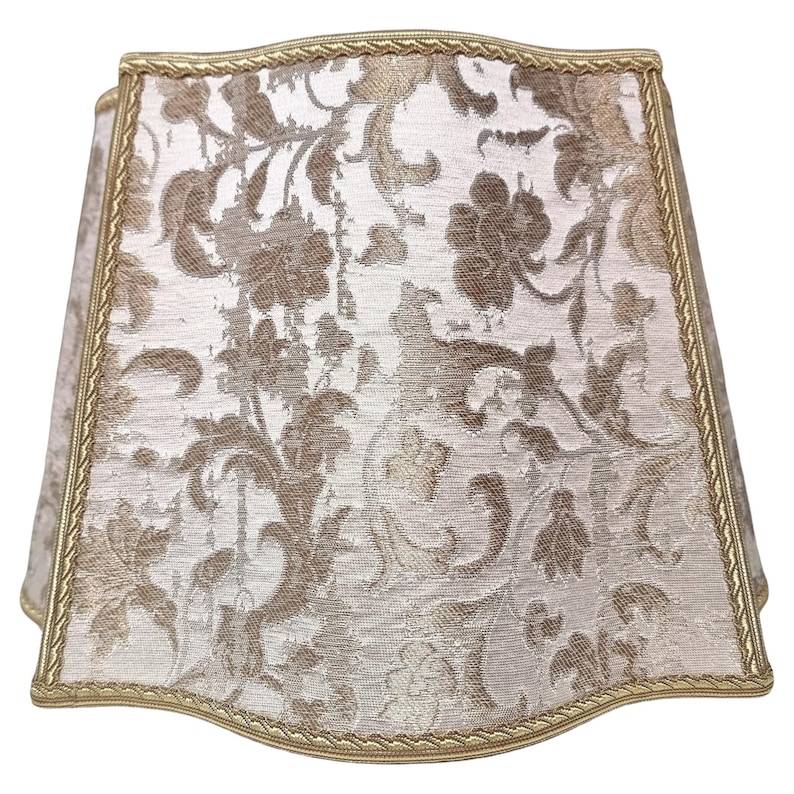 May include: A white lampshade with a gold trim and a floral pattern.