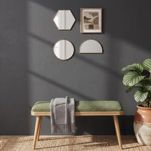May include: A wooden bench with a green upholstered seat and a grey textured throw blanket draped over it. Above the bench are three wall-mounted mirrors in hexagonal, circular, and semi-circular shapes, alongside a framed abstract textile art piece.