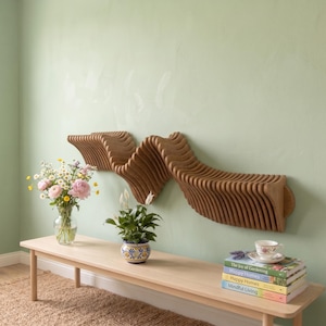 Op de afbeelding: Een wandplank van hout met een reeks verticale, golvende latten die een doorlopende golfvorm creëren. De plank is gemaakt van lichtbruin hout en is horizontaal bevestigd tegen een lichtgroene muur.
