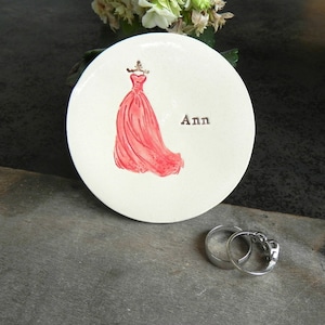 May include: White ceramic ring dish with a pink dress design and the name "Ann" written on it.