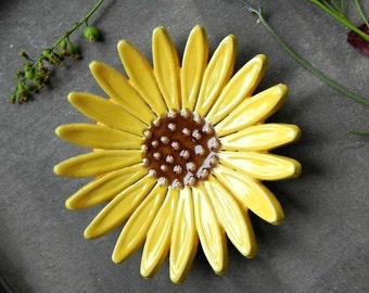 May include: A yellow ceramic sunflower dish with a brown center. The dish is on a gray background.