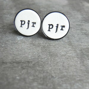 May include: Two white round cufflinks with a black border and the letters "pjr" in black.