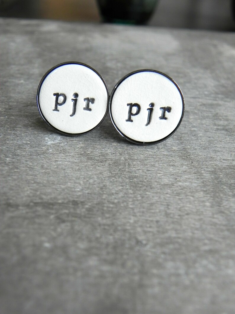 May include: Two white round cufflinks with a black border and the letters "pjr" in black.