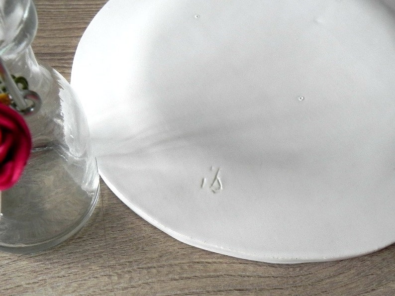 May include: White ceramic plate with a small, raised inscription that reads "ib".